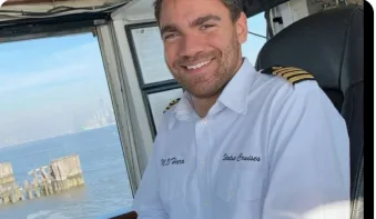 Matt O'Hara at a yacht's helm in a captain's shirt, the water visible through the bridge windows.